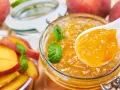 Un cucchiaio raccoglie la deliziosa marmellata di pesche da un barattolo, con pesche fresche e foglie di menta intorno.