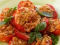 Pomodori al forno ripieni di pangrattato e erbe aromatiche, guarniti con basilico fresco.