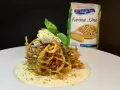Deliziosi spaghetti di zucchine fritte croccanti, serviti su una crema vellutata e guarniti con ricotta fresca e basilico.