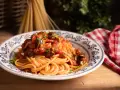 Piatto di spaghetti alla puttanesca, conditi con pomodoro, olive e capperi, guarniti con prezzemolo fresco.