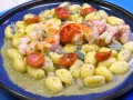 Gnocchi con pesto, gamberi succulenti e pomodorini confit. Un piatto che celebra i sapori del mare e della terra.