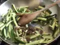 Zucchine in agrodolce veloci in padella con pinoli e uvetta, mescolate con un cucchiaio di legno.