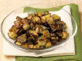 Melanzane a funghetto ricetta della nonna: cubetti dorati e saporiti, conditi con erbe aromatiche, in una ciotola di vetro.