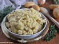 Un saporito piatto di patate in tecia, cotte con erbe aromatiche e spezie, servite in una ciotola su un tagliere di legno.
