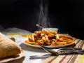 Piatto fumante di penne alla vodka, con pane croccante e posate pronte per gustare questo classico italiano.