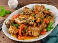 Un saporito coniglio in umido con carote e erbe aromatiche, servito su un piatto bianco.