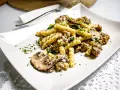 Un piatto di pasta salsiccia e funghi, condito con prezzemolo fresco, servito su un piatto bianco.