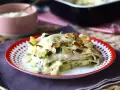 Una fetta di lasagne vegetariane con zucchine e besciamella, dorata al forno, servita su un piatto rosso e bianco.