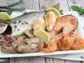 Un piatto invitante di grigliata di pesce: orata intera, tranci di salmone, gamberi, calamari e tonno, guarnito con limone e prezzemolo.