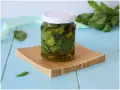 Un vasetto di basilico sott'olio, con foglie fresche sullo sfondo, pronto per insaporire i tuoi piatti.