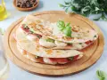 Piadina romagnola ripiena di prosciutto crudo, mozzarella e basilico, servita su un tagliere di legno.