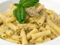 Un piatto di pasta con melanzane in bianco cremosa, condita con erbe aromatiche e guarnita con una foglia di basilico fresco.