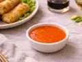 Una ciotola di salsa agrodolce arancione brillante, perfetta per accompagnare involtini primavera dorati.