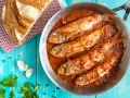 Triglie alla livornese in padella, con pane rustico, aglio e prezzemolo su tavolo blu.