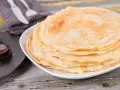 Pila di crepes senza uova, dorate e soffici, pronte per essere farcite. Accanto, un cucchiaino di marmellata.