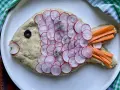 Pesce finto ricetta: un impasto cremoso decorato con ravanelli affettati, carote a bastoncino, un'oliva e erbe aromatiche.