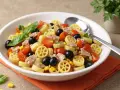 Un piatto invitante di pasta fredda tonno con pomodorini, olive nere, mais e basilico fresco. Perfetta per un pranzo estivo.