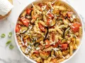 Un piatto invitante di pasta fredda alla norma con melanzane, pomodori e ricotta salata grattugiata.