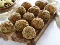 Deliziose polpette di verdure dorate e croccanti, disposte su un tagliere di legno. Un contorno di patate e piselli sullo sfondo.