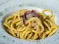 Un piatto di bigoli in salsa, con pasta spessa e condimento a base di acciughe e cipolla, guarnito con prezzemolo tritato.