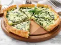 Una fetta di torta rustica ricotta e spinaci, con crosta dorata e ripieno cremoso, guarnita con basilico fresco.