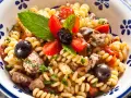 Fusilli con pesce spada, pomodorini, olive nere e menta fresca in una ciotola decorata.