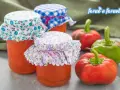 Barattoli di salsa di peperoni fatti in casa, decorati con stoffe floreali e a quadretti, accanto a peperoni freschi.