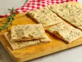 Focaccia senza lievito, croccante e profumata al rosmarino, servita su un tagliere di legno con un tovagliolo a quadri rossi.