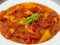 Un piatto di peperonata ricetta, con peperoni rossi e gialli cotti in salsa, guarnito con basilico fresco.