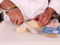 Mani che tagliano un pezzo di Parmigiano Reggiano, pronto per una deliziosa fonduta.
