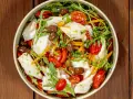 Insalata di calamari fresca con pomodorini, olive, rucola e carote julienne, un piatto leggero e saporito.