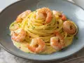 Un piatto di tagliolini al limone con gamberi succulenti, guarnito con erbe aromatiche e pepe rosa.