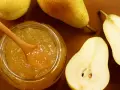 Un vasetto di confettura di pere con un cucchiaio di legno, circondato da pere fresche, alcune intere e altre tagliate a metà.