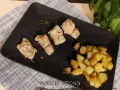 Pezzi di baccalà al forno con rosmarino e patate arrosto su piatto nero.