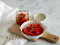 Peperoni sott'olio in una ciotola e in un barattolo, pronti per essere gustati. Un rametto di rosmarino decora i peperoni.