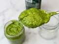 Cucchiaio pieno di pesto senza pinoli, cremoso e verde brillante, accanto a un barattolo.