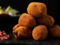 Pile di supplì alla carbonara dorati e croccanti, con guanciale a cubetti e insalata sfocata sullo sfondo.