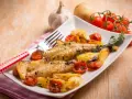 Piatto di coda di rospo al forno con patate arrosto e pomodorini. Un contorno di erbe aromatiche completa il piatto.