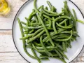 Un piatto di fagiolini lessi, freschi e verdi, pronti per essere gustati. Accanto, un piccolo recipiente con olio d'oliva.