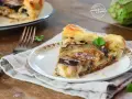 Una fetta di torta salata con melanzane, formaggio filante e pasta sfoglia dorata, guarnita con prezzemolo fresco.