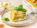 Una fetta di parmigiana di zucchine, stratificata e dorata, guarnita con basilico fresco.