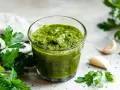 Un bicchiere di vibrante salsa verde, con prezzemolo fresco e spicchi d'aglio sullo sfondo.
