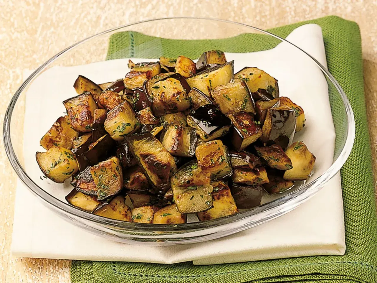 Melanzane a funghetto ricetta della nonna: cubetti dorati e saporiti, conditi con erbe aromatiche, in una ciotola di vetro.