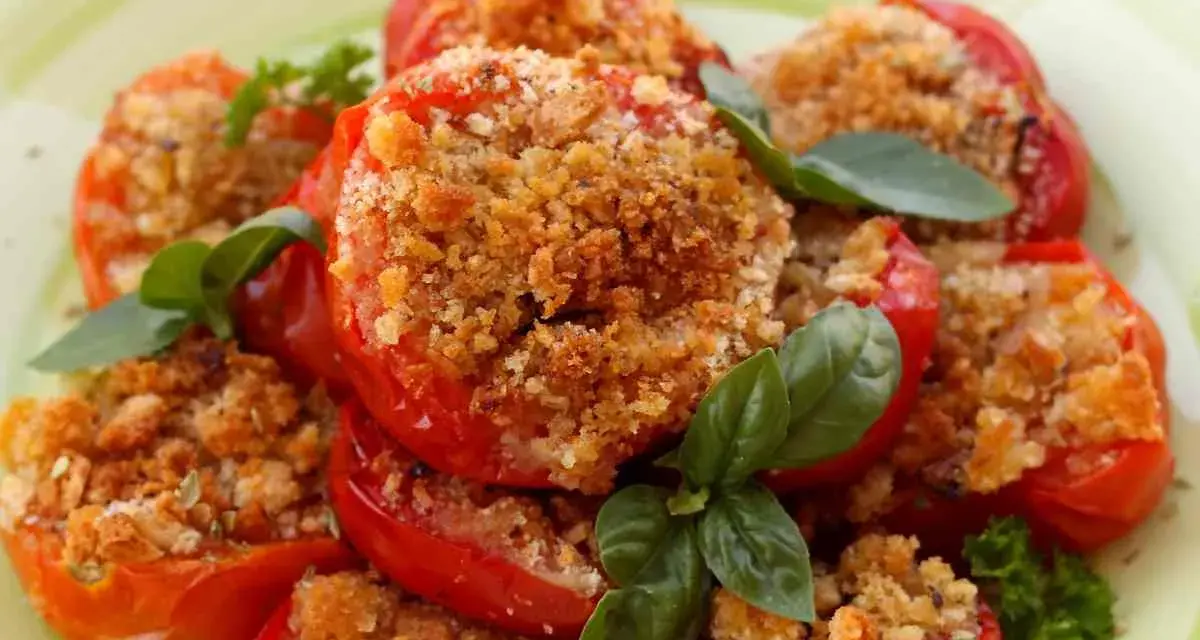 Pomodori al forno ripieni di pangrattato e erbe aromatiche, guarniti con basilico fresco.