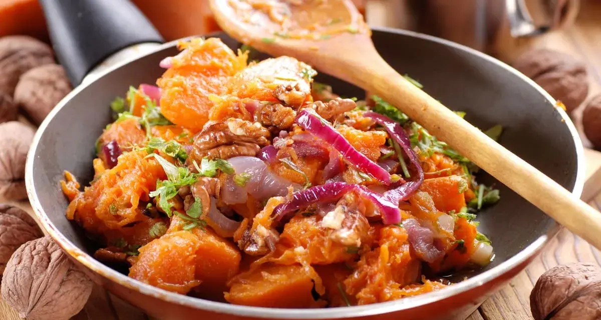 Deliziosa zucca in padella con cipolla rossa e noci, guarnita con erbe fresche. Un piatto autunnale invitante.