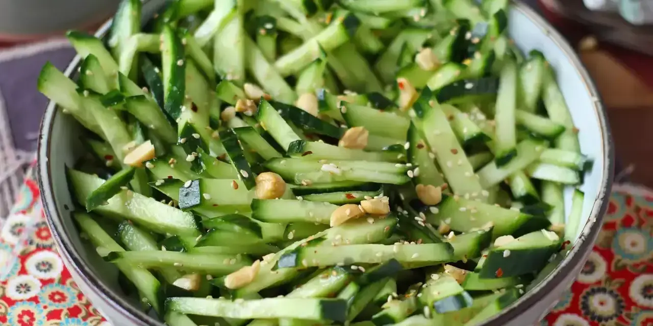 Una ciotola piena di fresca insalata di cetrioli tagliati a julienne, condita con semi di sesamo e arachidi croccanti.