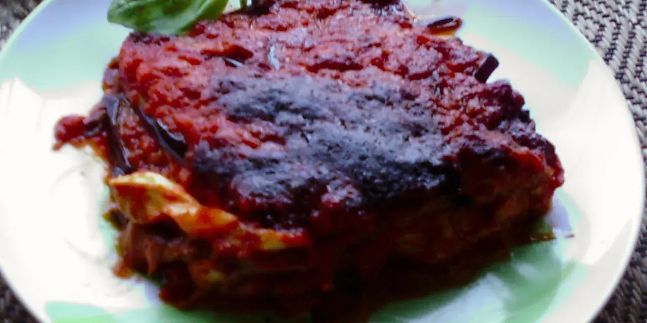 Una porzione di parmigiana di melanzane napoletana, ricca e saporita, guarnita con basilico fresco.