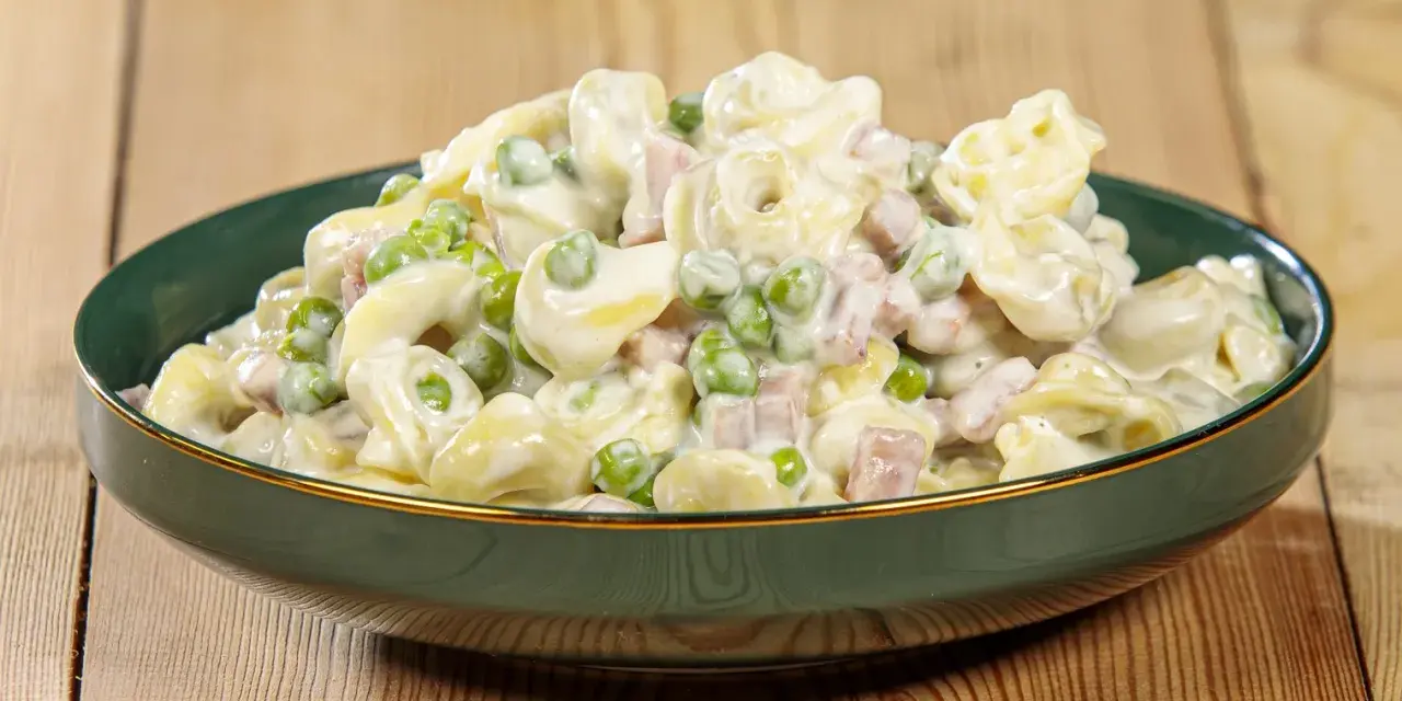 Un piatto invitante di tortellini panna e prosciutto, con piselli verdi, conditi con una cremosa salsa bianca.