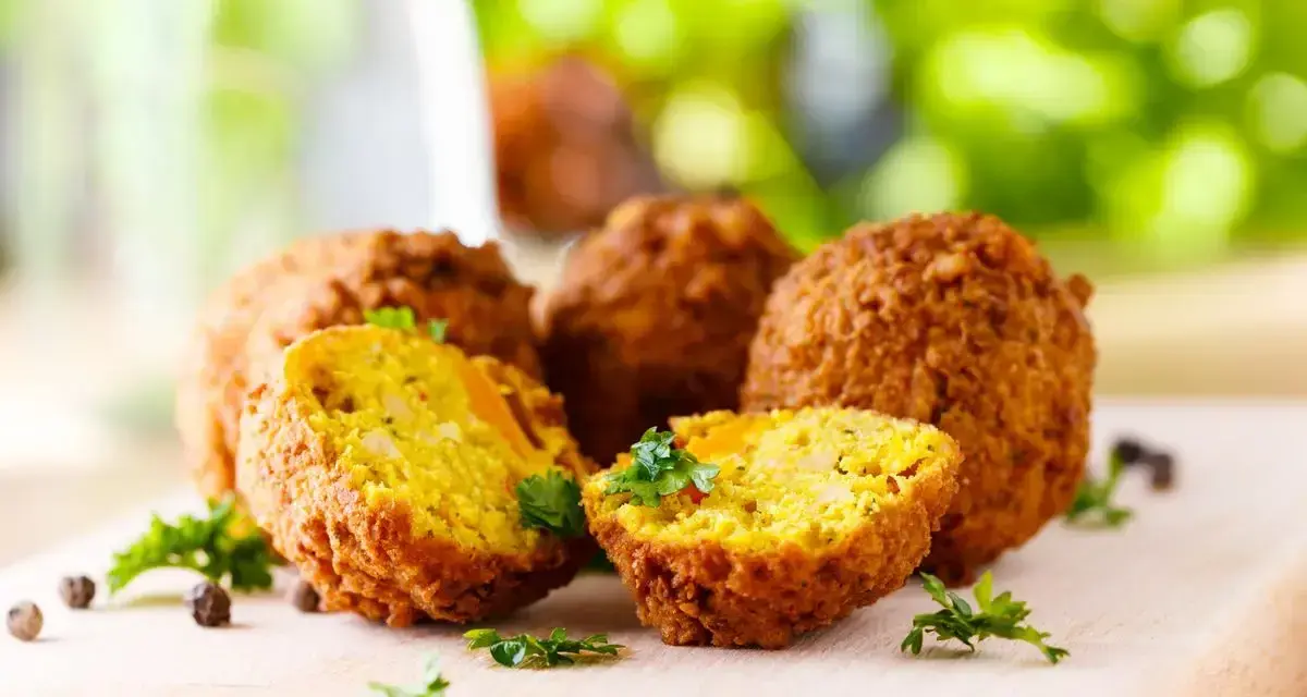 Polpette di ceci dorate e croccanti, cotte in friggitrice ad aria, guarnite con prezzemolo fresco su tagliere di legno.