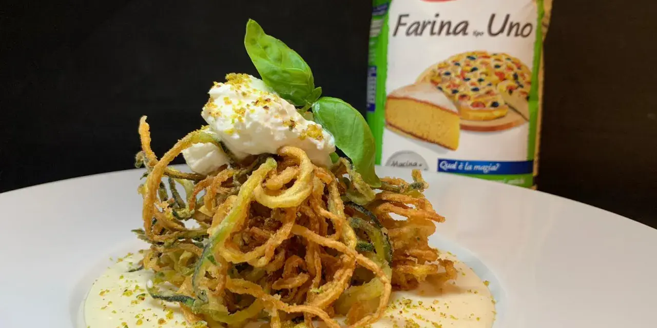 Deliziosi spaghetti di zucchine fritte croccanti, serviti su una crema vellutata e guarniti con ricotta fresca e basilico.